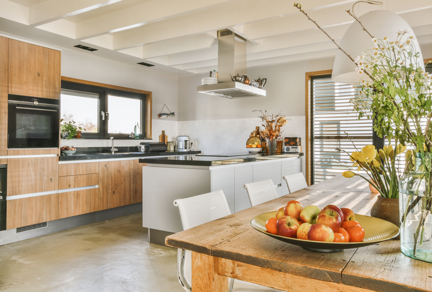 Modern minimalist style interior design of studio apartment with open white kitchen and dining zone with table and chairs illuminated by loft style lamp