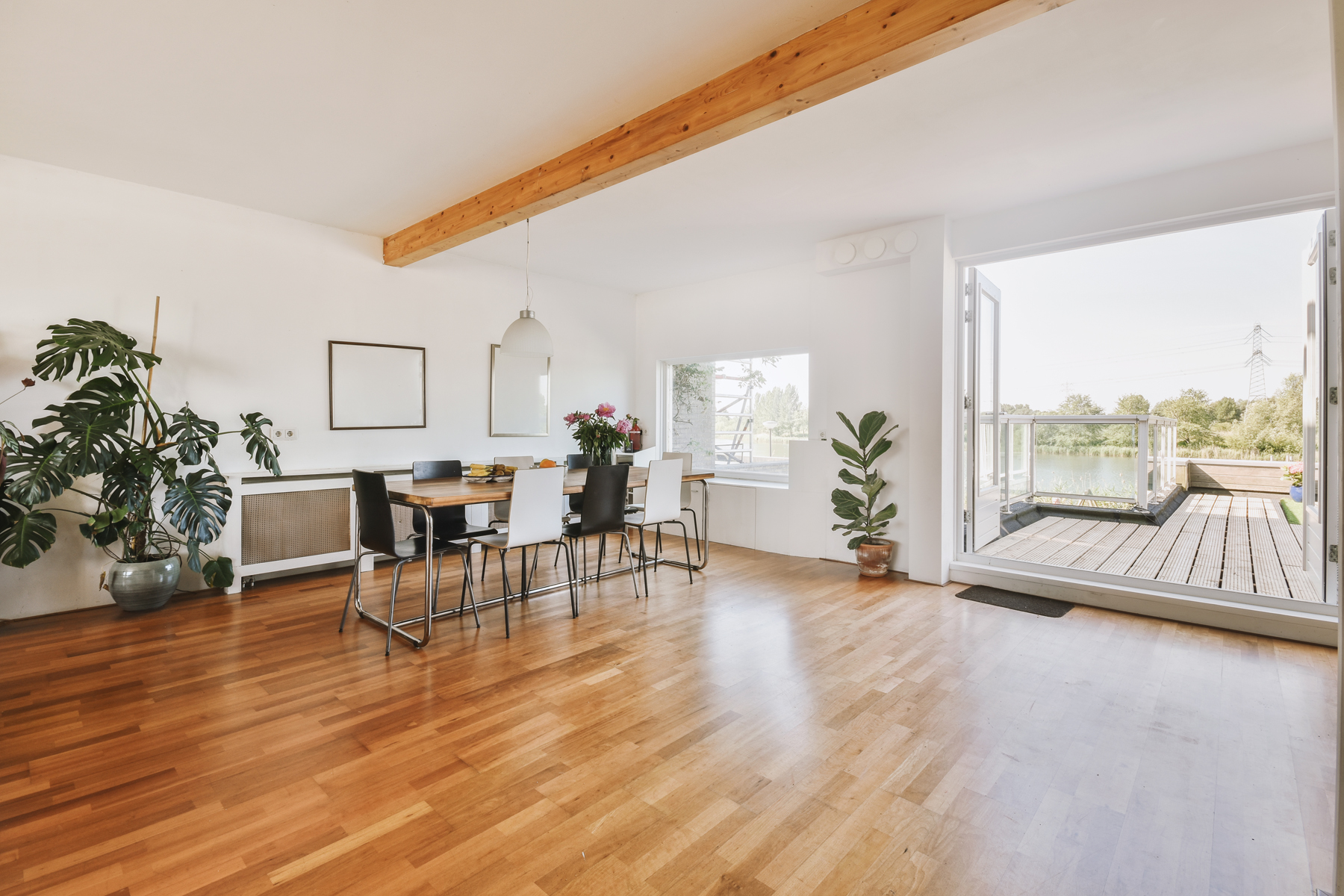 Contemporary minimalist style interior design of light studio apartment with wooden table and chairs in dining zone between open kitchen and living room with white walls and parquet floor